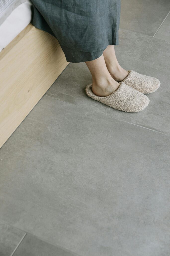 Two tan slippers on a woman's feet on a tile floor
