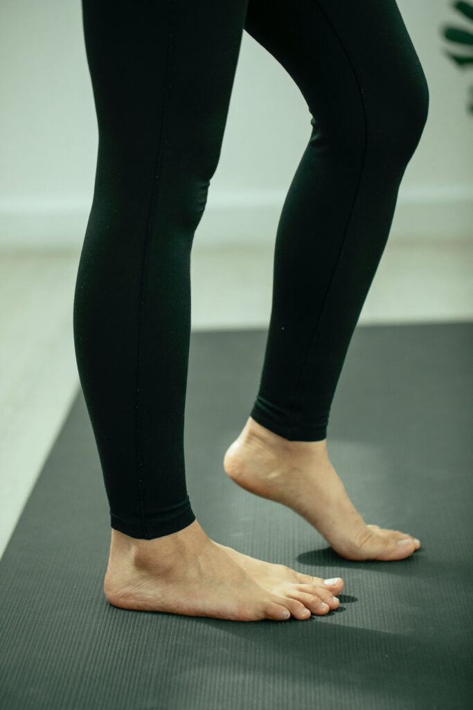 A woman in yoga pants. Two bare feet on a yoga mat.
